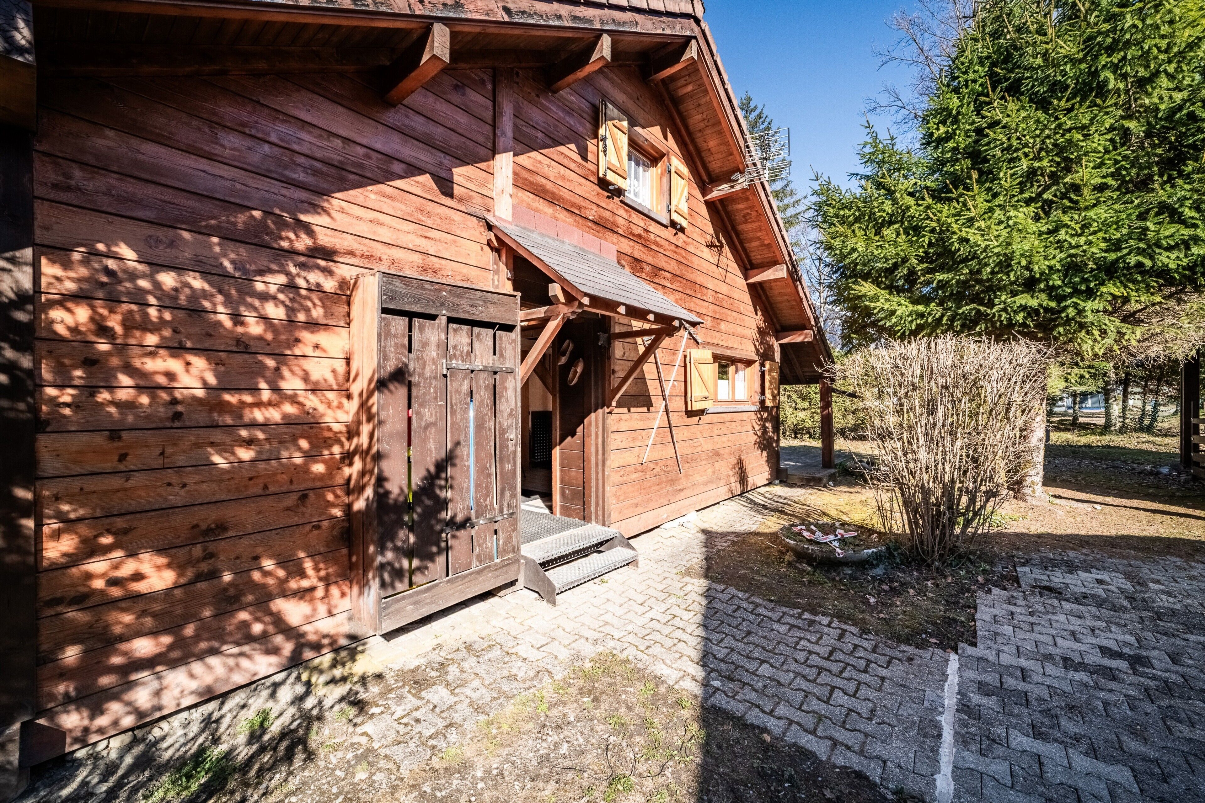 Une cabane en bois avec une porte en bois, un petit porche et un chemin de briques menant à l’entrée.