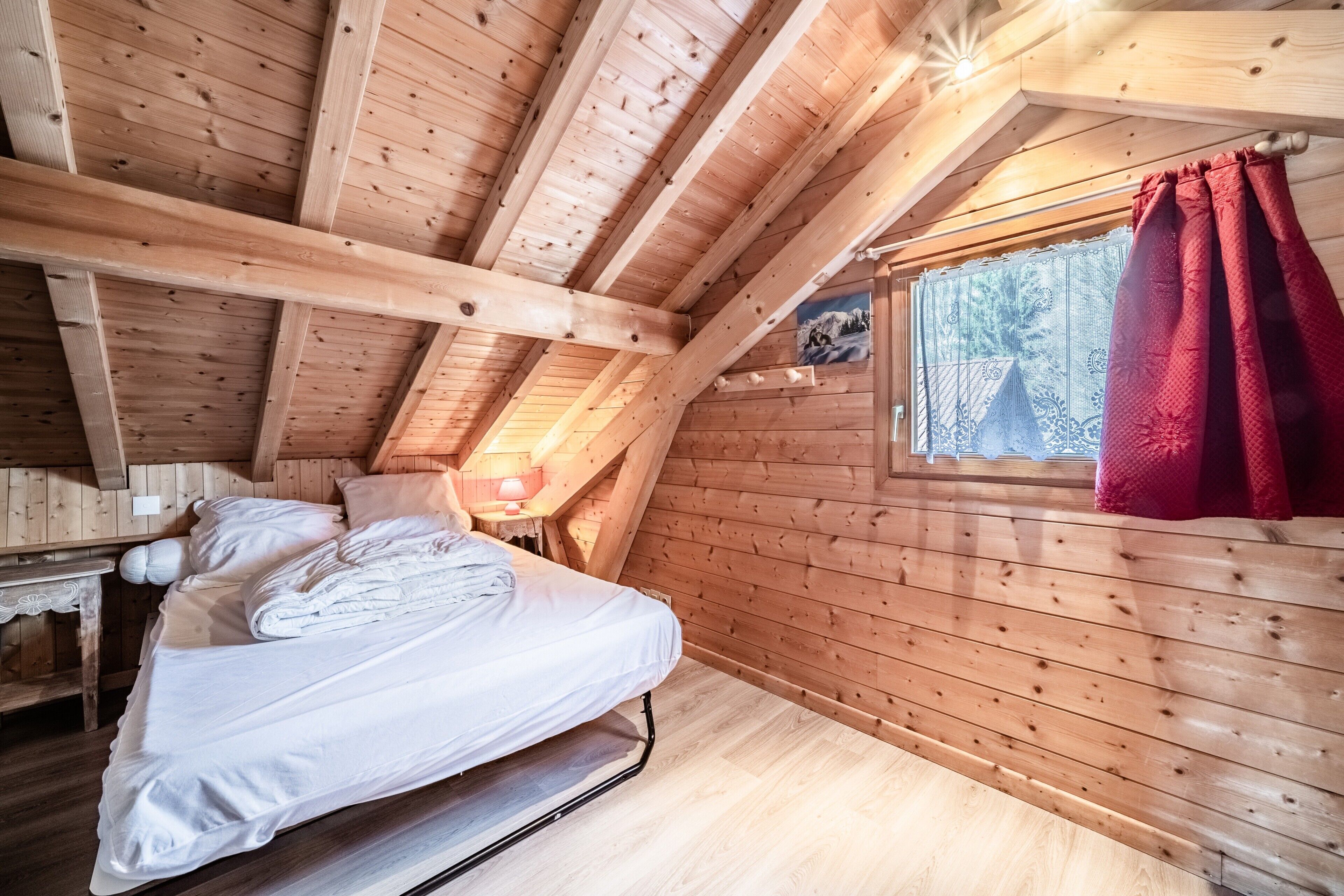 Una habitación de cabaña de madera con una cama, un ventanal y una cortina roja.