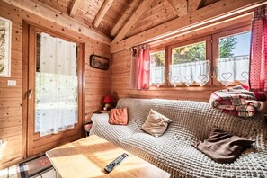 A cozy cabin interior with a wooden ceiling, a sofa with a blanket, a remote control on a table, and heart-patterned curtains. - Chalet '7p Comfort - Le Refuge' with Mountain View, Private Terrace and Wi-Fi (Verchaix)