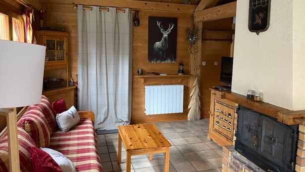 L’intérieur d’un chalet accueillant, avec un plafond en bois, un canapé, une table, une cheminée et un tableau représentant un cerf.
