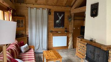 Interior acogedor de una cabaña con techo de madera, un sofá, una mesa, una chimenea y un cuadro de un ciervo.