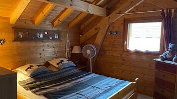 Un dormitorio acogedor de cabaña de madera con cama, cómoda y ventana.
