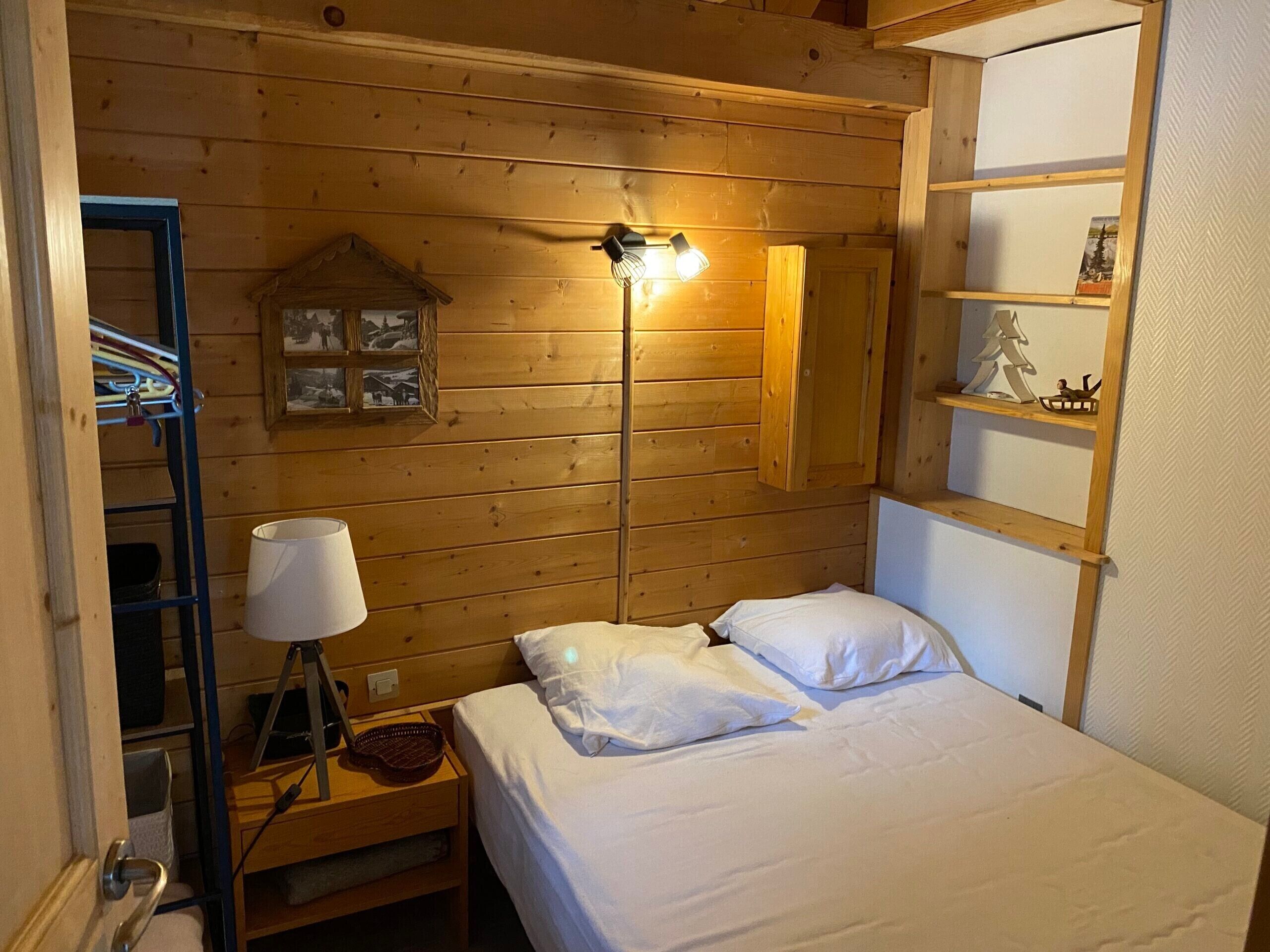 Una camera in stile baita con un letto, un comodino, una lampada, uno scaffale con un addobbo natalizio e un quadro appeso al muro.