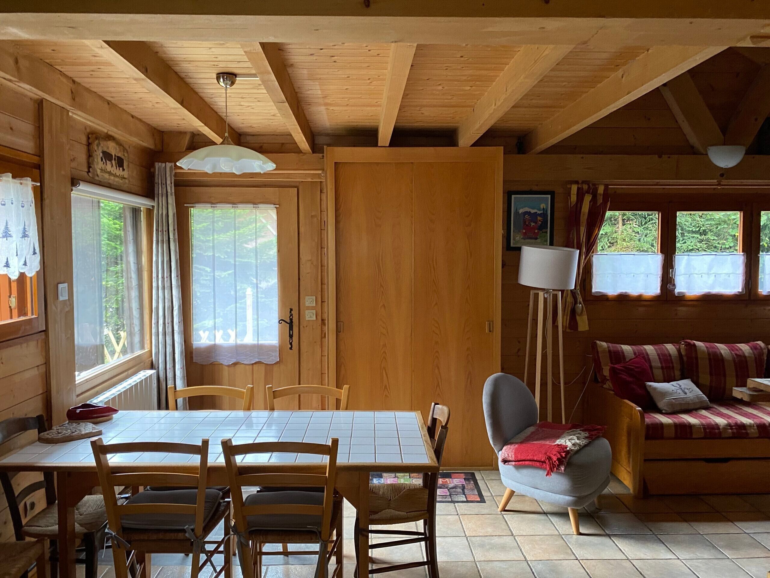 Interior de una cabaña de madera con una mesa de comedor, sillas, un sofá y una lámpara.