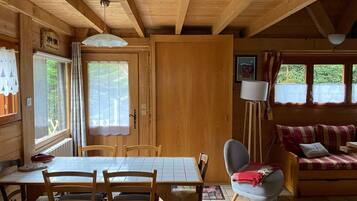 Interior de una cabaña de madera con una mesa de comedor, sillas, un sofá y una lámpara.