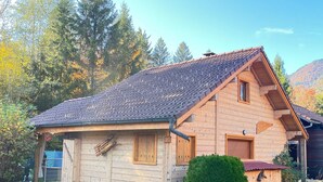 A wooden cabin with a sloped roof, a covered porch, and a small garden area. - Chalet “6p Comfort - Le Chevreuil”: Mountain View, Private Terrace & Wi-Fi (Verchaix)
