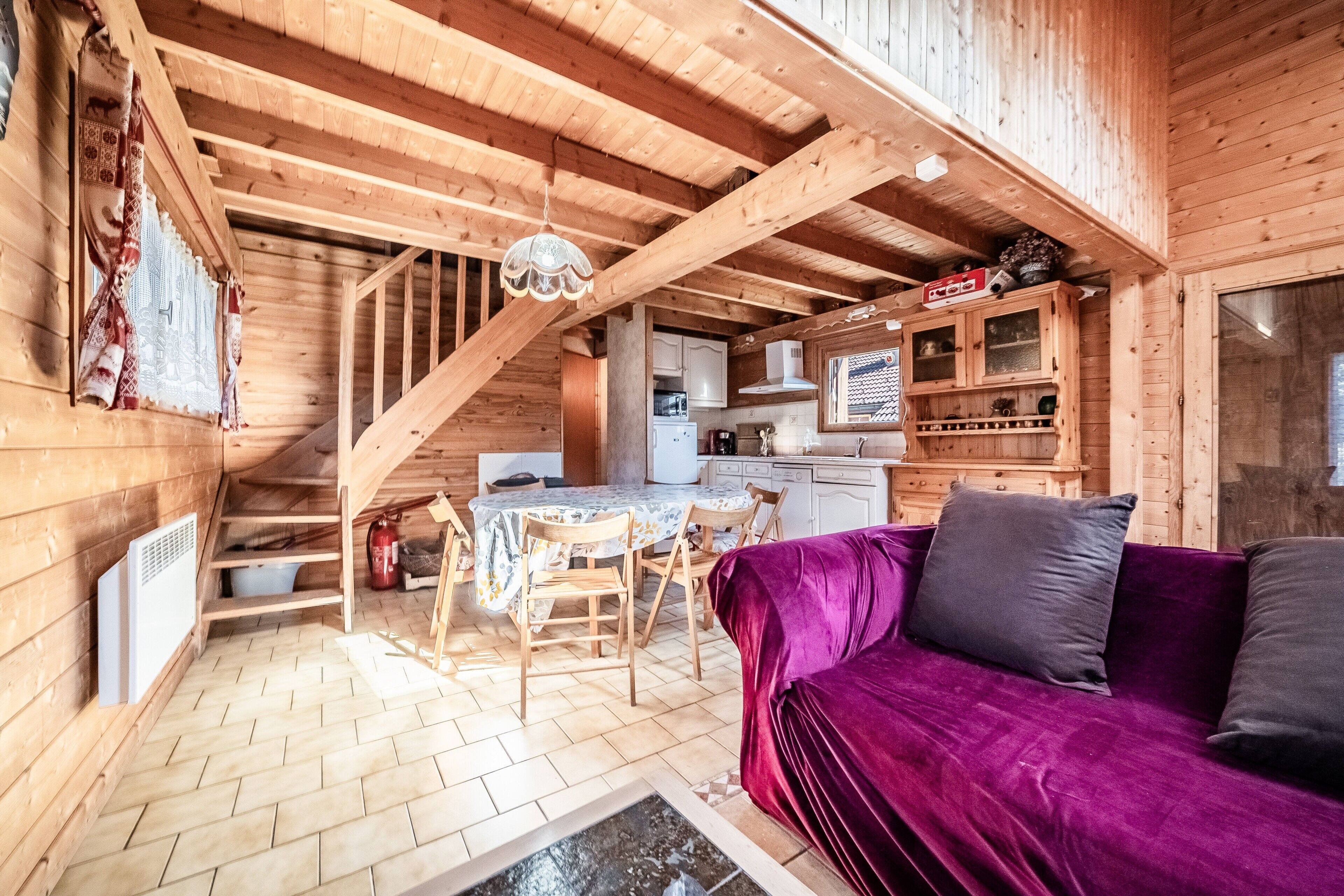 Interior de una cabaña de madera con comedor, cocina y un sofá púrpura.