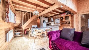 A wooden cabin interior with a dining area, kitchen, and a purple sofa.