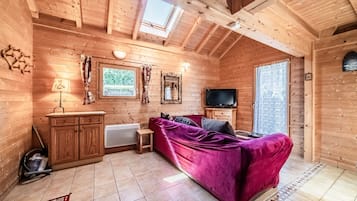 A wooden cabin interior with a sofa, television, and a window.