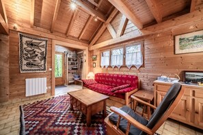 A wooden cabin interior with a sofa, a table, a chair, a radiator, and a window with a view. - Chalet “6p Comfort - Les Cerfs”: Mountain View, Private Terrace & Wi-Fi (Verchaix)