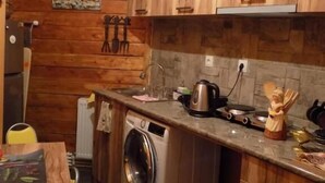 A compact kitchen with wooden cabinets, a washing machine, a sink, and a countertop with various kitchen items. - City Guli Hostel (Tbilisi)