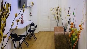 A modern living room with a wooden floor, a sofa, a TV mounted on the wall, and decorative plants. - City Guli Hostel (Tbilisi)