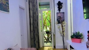 A cozy living room with a sofa, a dining table with chairs, a TV mounted on the wall, and a door leading to a balcony. - City Guli Hostel (Tbilisi)