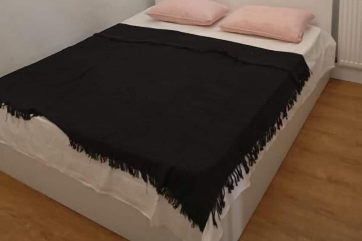 Ein Schlafzimmer mit einem weißen Bett, zwei rosafarbenen Kissen, einer schwarzen Decke und einem Gemälde einer Tänzerin an der Wand.