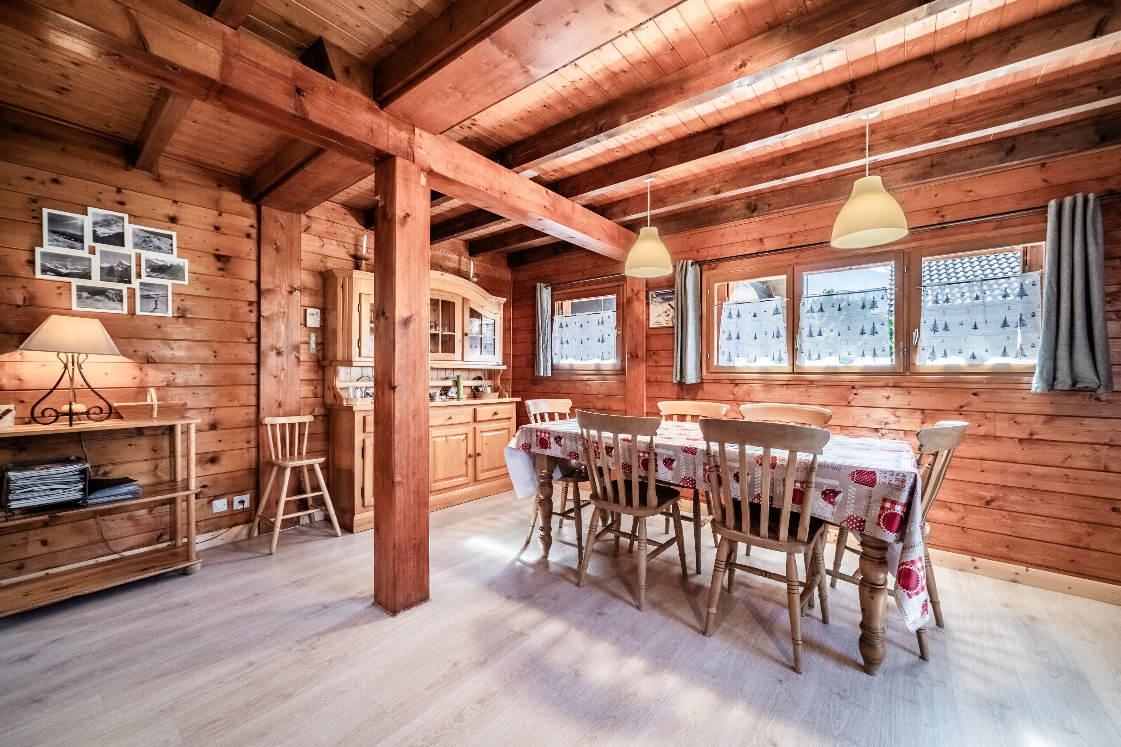 Un interior de madera con una mesa de comedor, sillas, una lámpara, un estante y una ventana con cortinas.