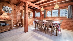 A wooden interior with a dining table, chairs, a lamp, a shelf, and a window with curtains. - Chalet “6p Comfort - L’ours Blanc”: Mountain View, Private Garden & Wi-Fi (Verchaix)