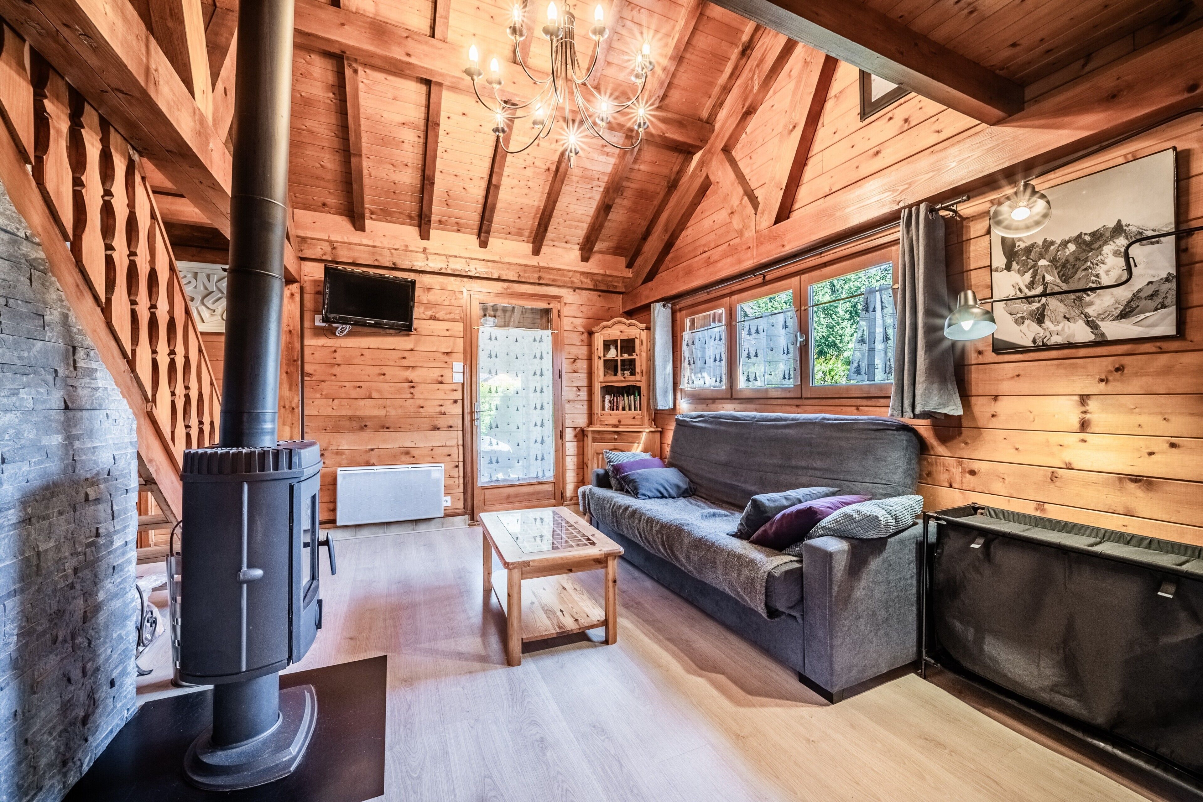 Interior acogedor de una cabaña con estufa de leña, sofá, mesa y televisor.