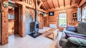 A wooden cabin interior with a fireplace, sofa, table, and a TV mounted on the wall. - Chalet “6p Comfort - L’ours Blanc”: Mountain View, Private Garden & Wi-Fi (Verchaix)