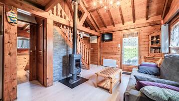 A wooden cabin interior with a fireplace, sofa, table, and a TV mounted on the wall.