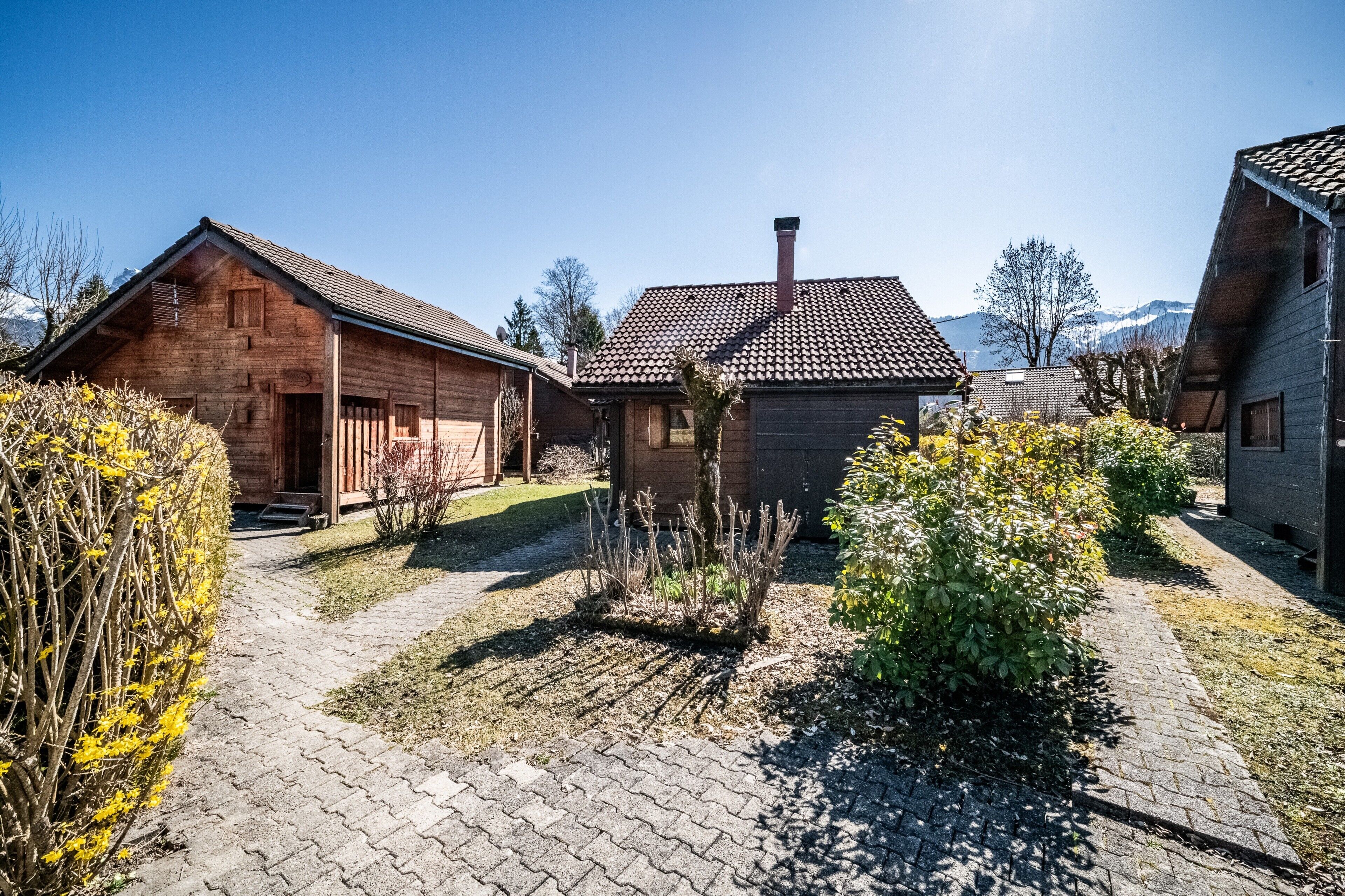 Une cabane en bois avec un toit en tuiles, entourée d’un chemin pavé et agrémentée d’un petit jardin.