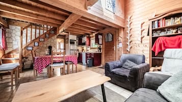 A wooden interior with a dining area, a sofa, and a kitchen visible through an open door.