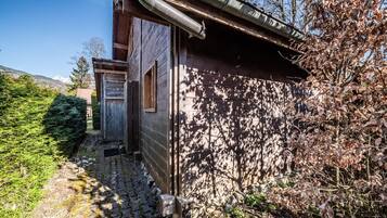 Un edificio rústico de madera con techo metálico, un sendero de piedra y follaje circundante.