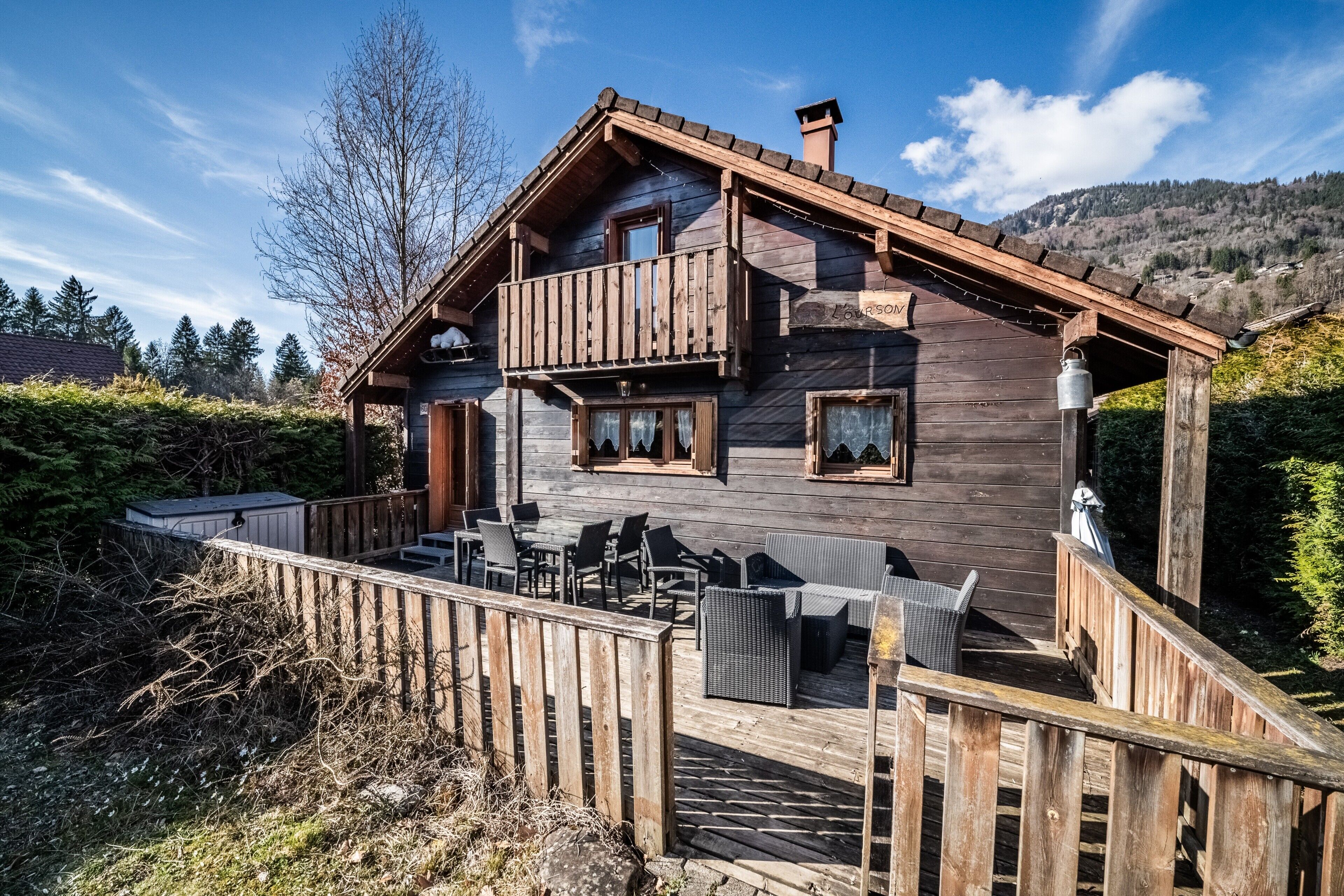 Una cabaña de madera con balcón, mobiliario exterior y vistas del bosque circundante.