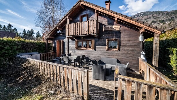 Una cabaña de madera con balcón, mobiliario exterior y vistas del bosque circundante.