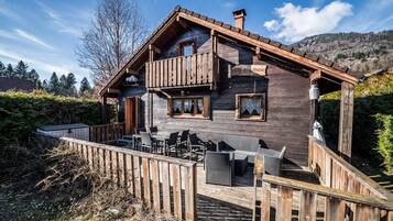 Una cabaña de madera con balcón, mobiliario exterior y vistas del bosque circundante.