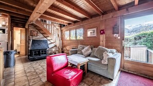 Interior de una cabaña de madera con chimenea, un sillón rojo, un sofá y vistas a la montaña.