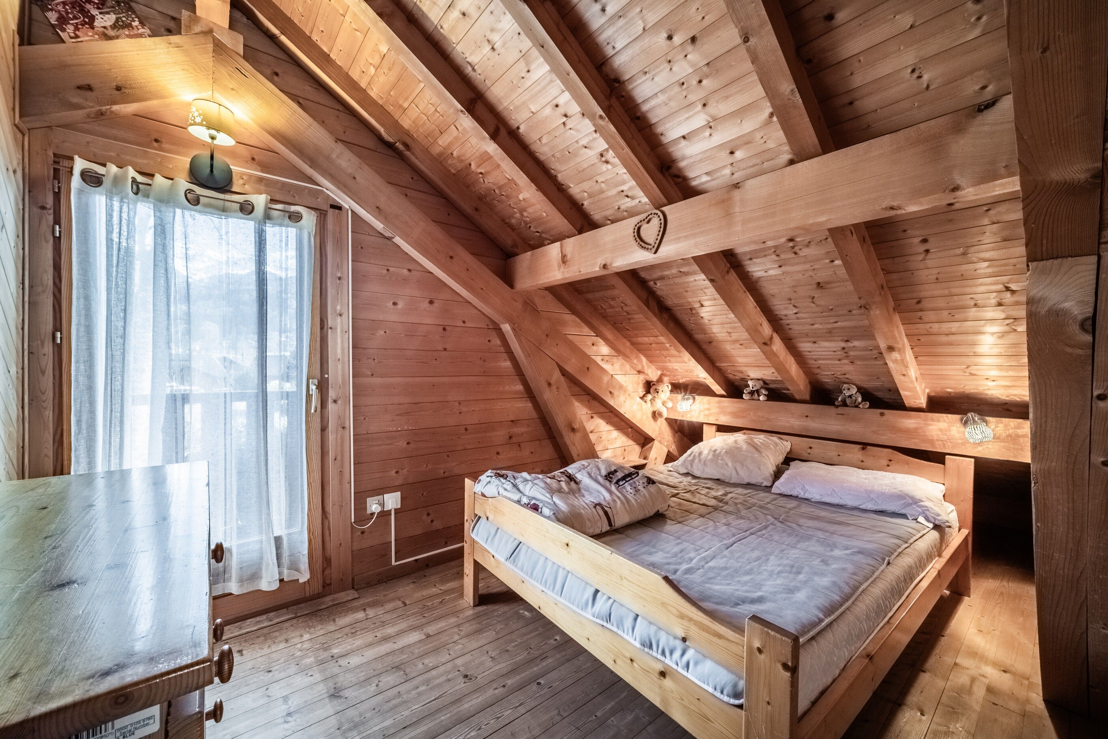 Ein Zimmer mit Holzboden, einem Bett, einem Tisch und einem Fenster mit Vorhängen.