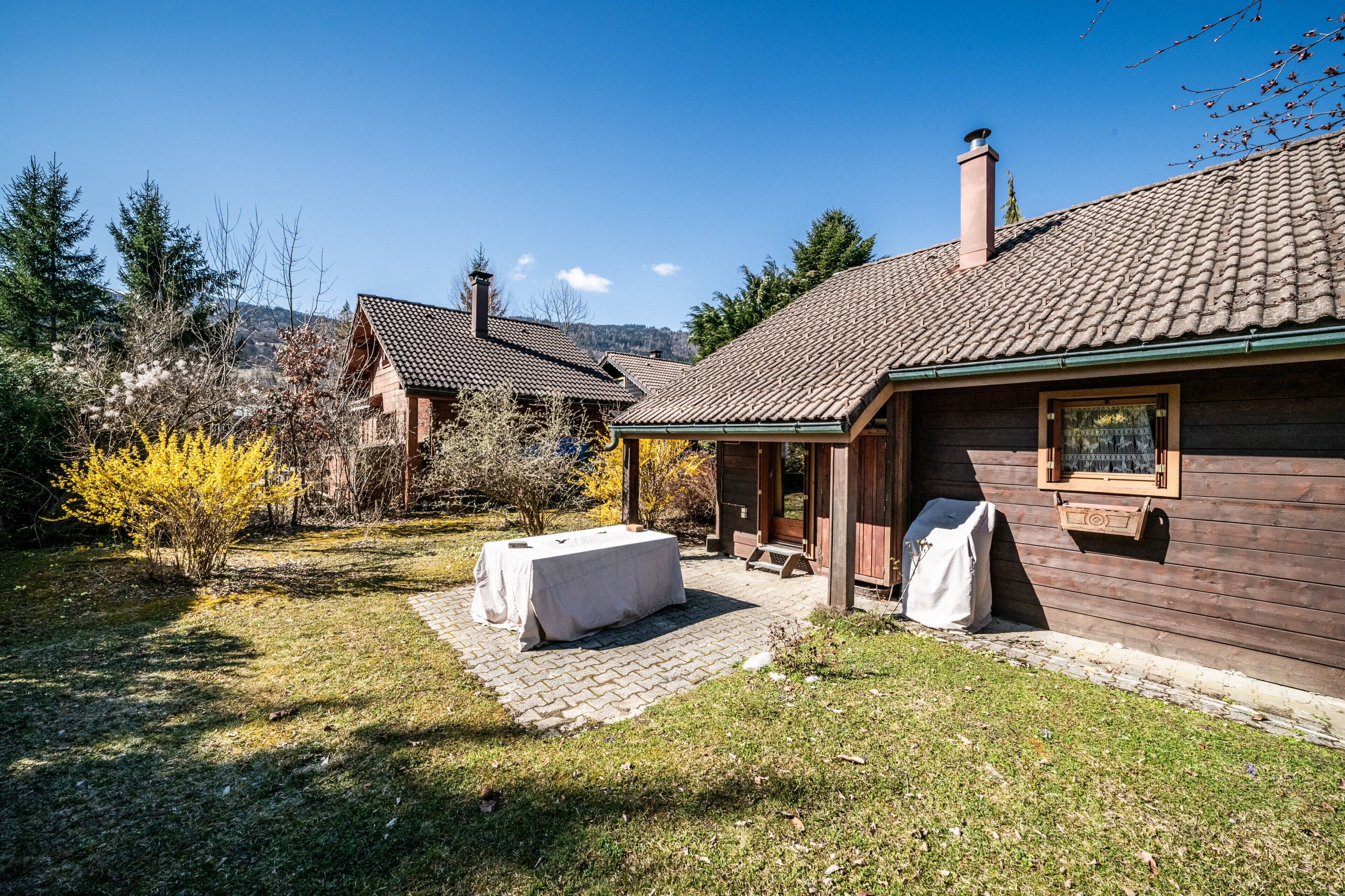 Ein Holzhaus mit Ziegeldach und einer überdachten Terrasse, an der ein Tisch draußen steht.