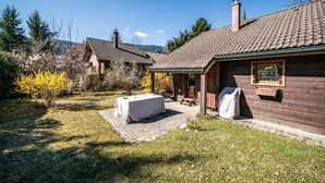 Une maison en bois avec un toit en tuiles, une terrasse couverte et une table dressée à l’extérieur.