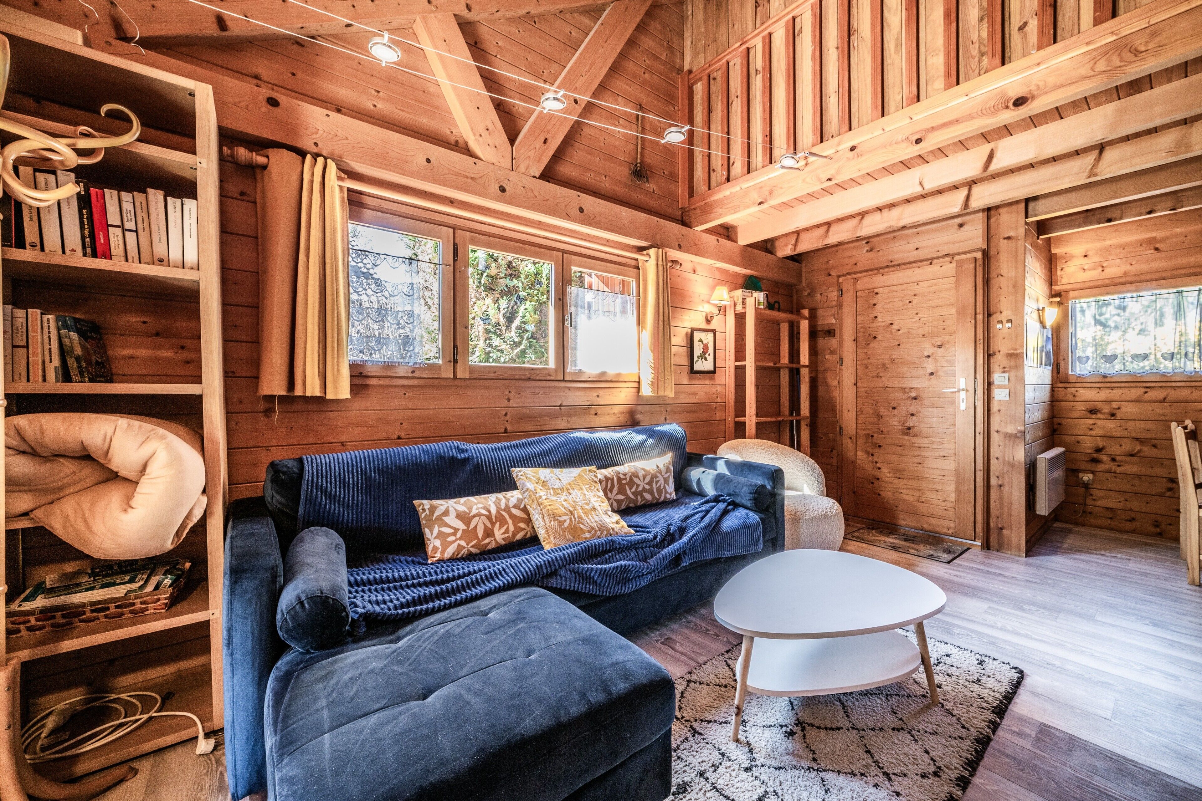 A wooden cabin interior with a sofa, a round table, and a bookshelf.