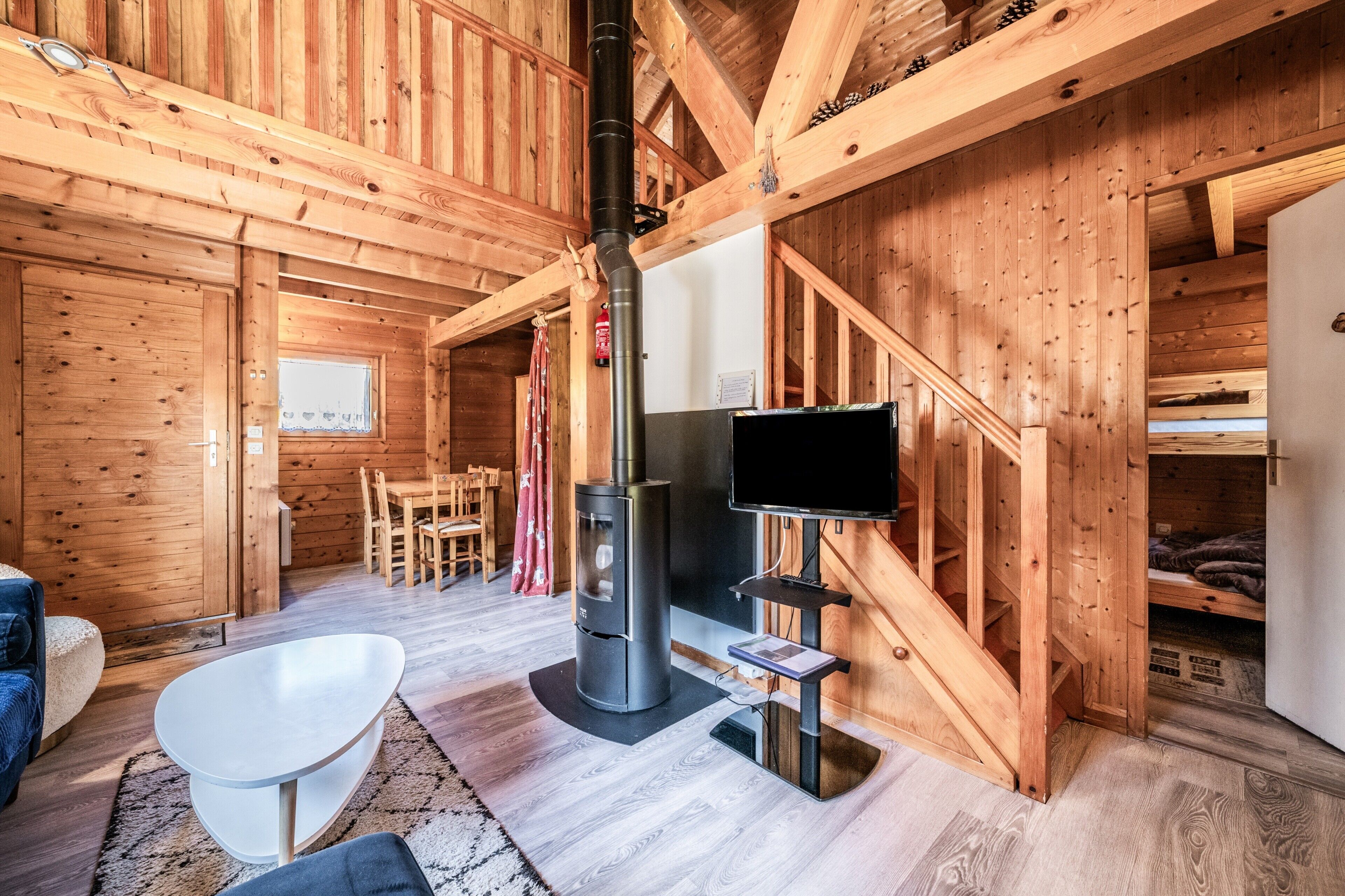 A wooden cabin interior with a fireplace, a flat-screen TV, a dining area, and a cozy seating arrangement.