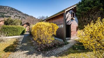 Eine Holzhütte mit Backsteinfassade, umgeben von einem Kopfsteinpflasterweg und gelb blühenden Sträuchern.