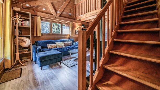 Un intérieur en bois avec un escalier, un canapé bleu et une bibliothèque.