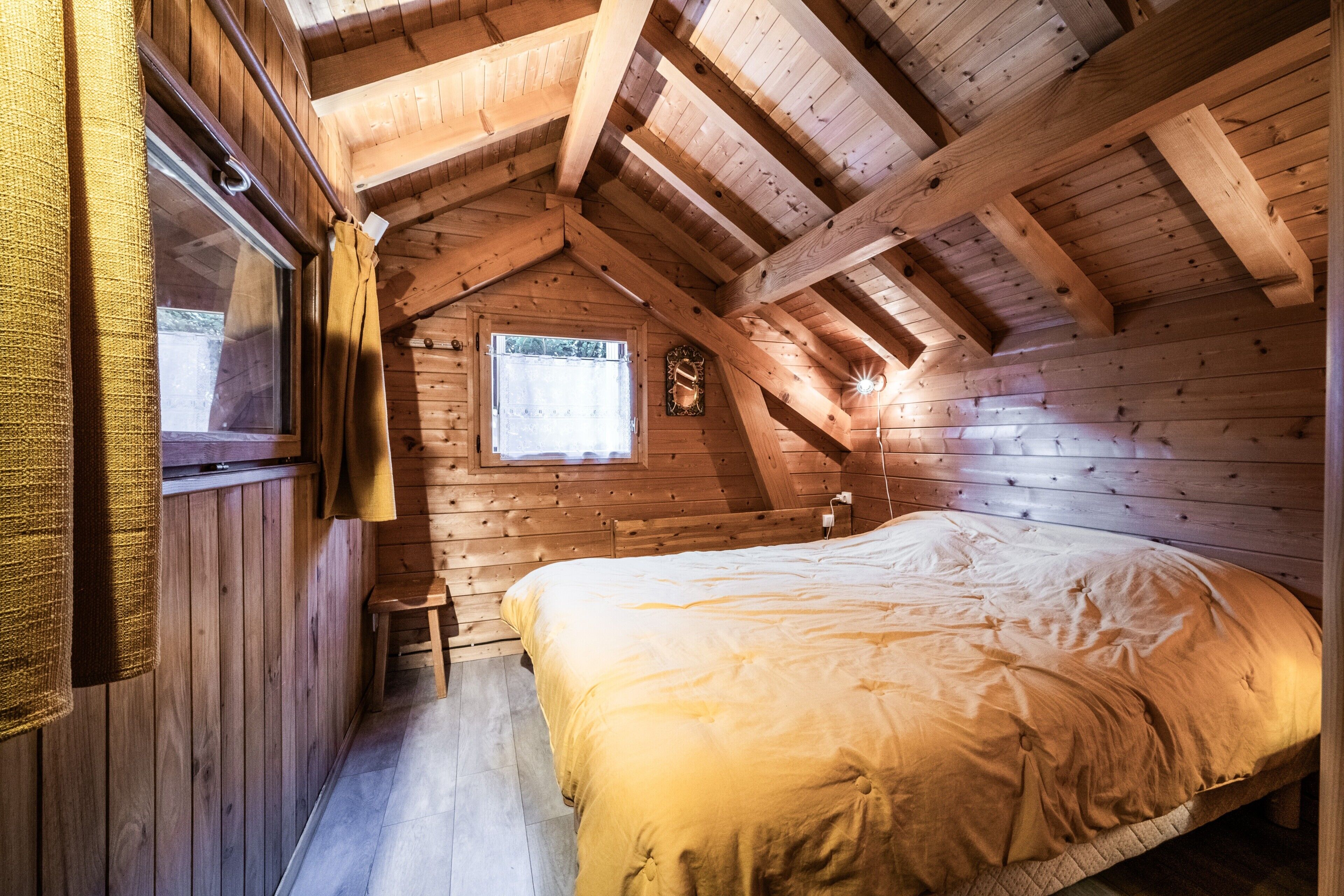 A wooden cabin bedroom with a bed, a window, and a small stool.
