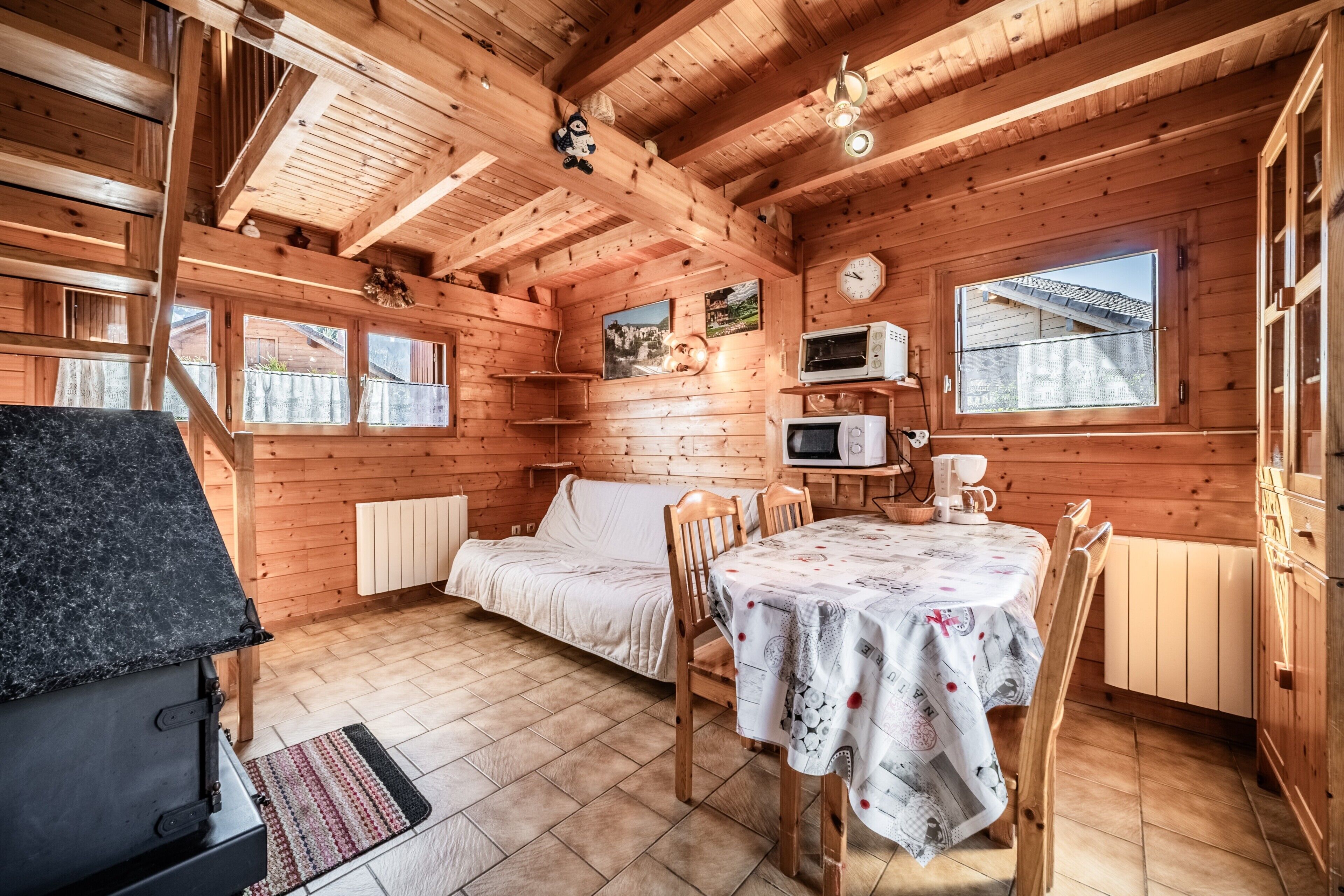 L'interno di una baita in legno con un letto, un tavolo, sedie, un forno a microonde, una sveglia e una finestra.
