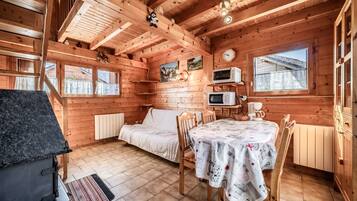 L'interno di una baita in legno con un letto, un tavolo, sedie, un forno a microonde, una sveglia e una finestra.