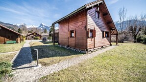 Een houten chalet met schuin dak, een geplaveid pad en een berg op de achtergrond.
