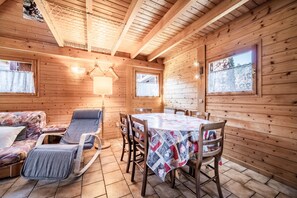 Ein Holzblockhaus-Interieur mit Esstisch, Stühlen, einer Couch und einem Fenster.