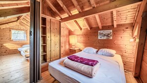Een slaapkamer in een houten blokhut met een bed, nachtkastje, lamp en raam.