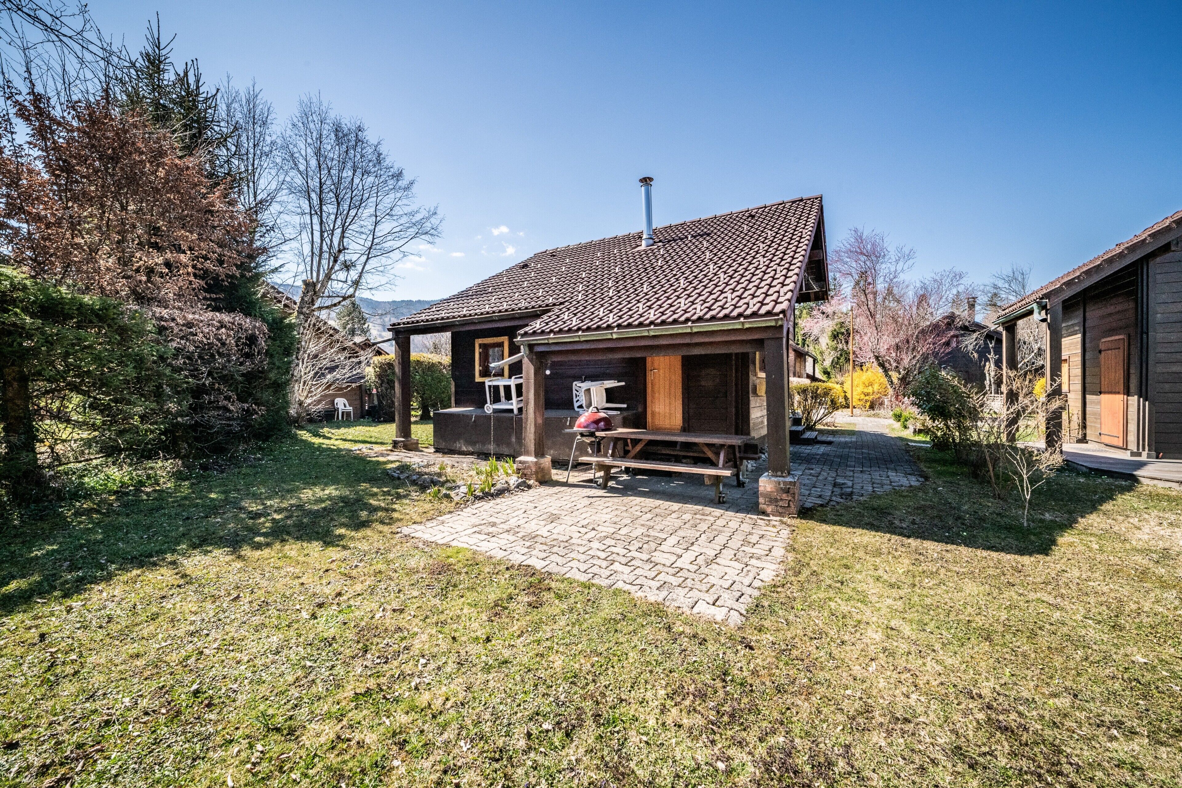 Una baita rustica con tetto in tegole, un patio in legno e un vialetto in mattoni che conduce all'ingresso.