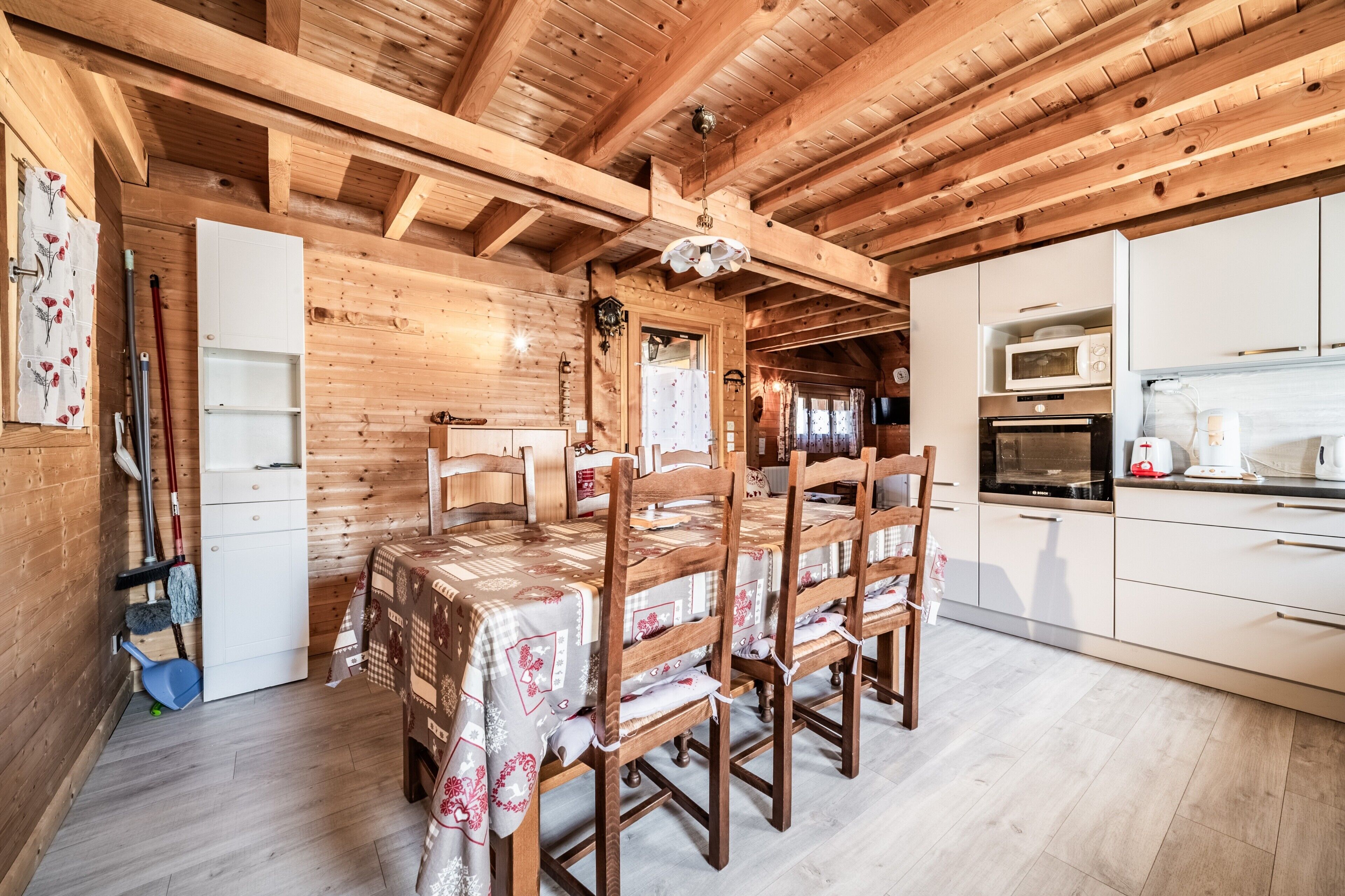 Un interno in legno con un tavolo da pranzo e sedie, una cucina con mobili e elettrodomestici bianchi, e un soffitto in legno.