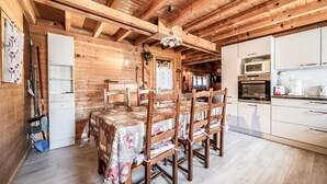 A wooden interior with a dining table and chairs, a kitchen with white cabinets and appliances, and a wooden ceiling. - Chalet “6p Comfort – Le Grand Tétras”: Mountain View, Private Terrace & Wi-Fi (Verchaix)