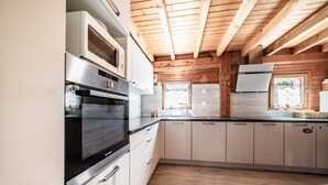 A modern kitchen with stainless steel appliances, wooden ceiling beams, and a view of the outdoors. - Chalet “6p Comfort – Le Grand Tétras”: Mountain View, Private Terrace & Wi-Fi (Verchaix)