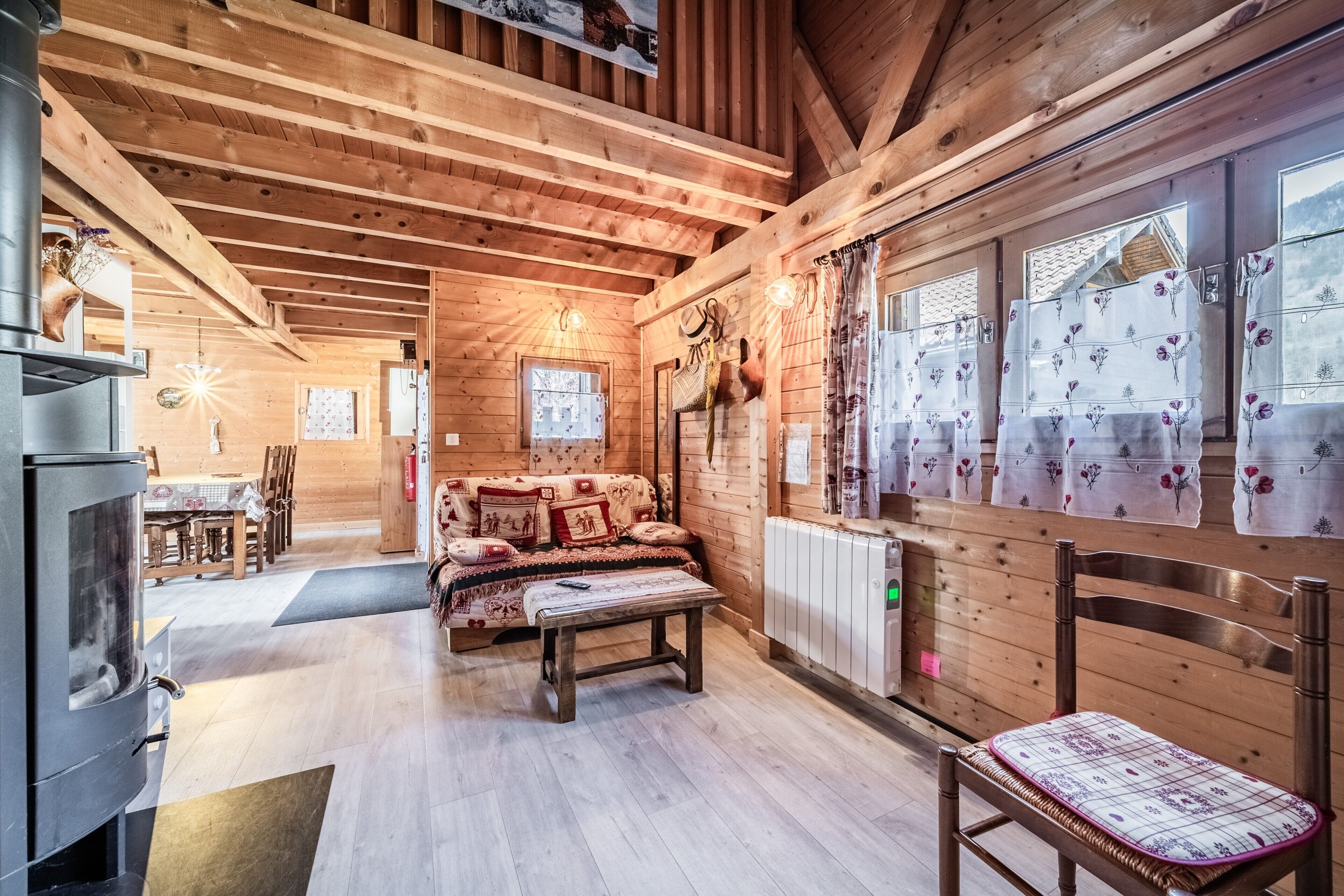 Interior acogedor de una cabaña de madera con sofá, mesa, silla y ventana con cortinas.