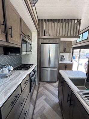 A modern kitchen with stainless steel appliances, wooden cabinets, and a herringbone floor pattern.