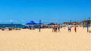 A beach volleyball court with players, tents, and beachgoers.